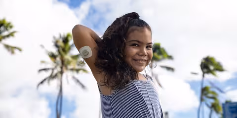 child wearing glucose sensor with palm trees in background