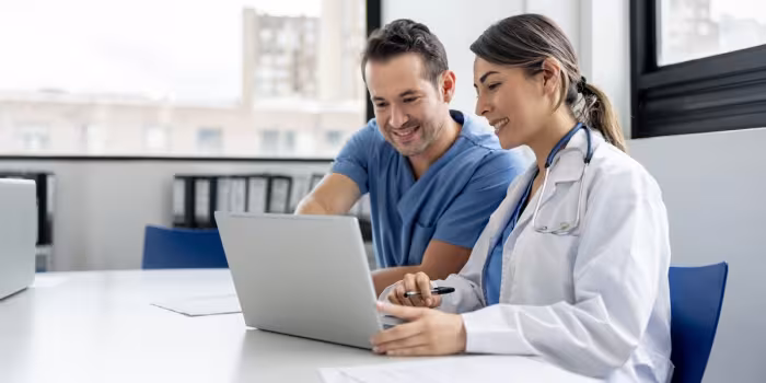 woman in white jacket looking at computer with man in blue scrubs