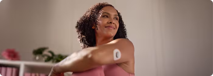 A woman wearing a continuous glucose monitor on her upper arm.