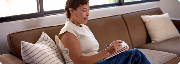 A woman sitting on a couch writing in a notebook.