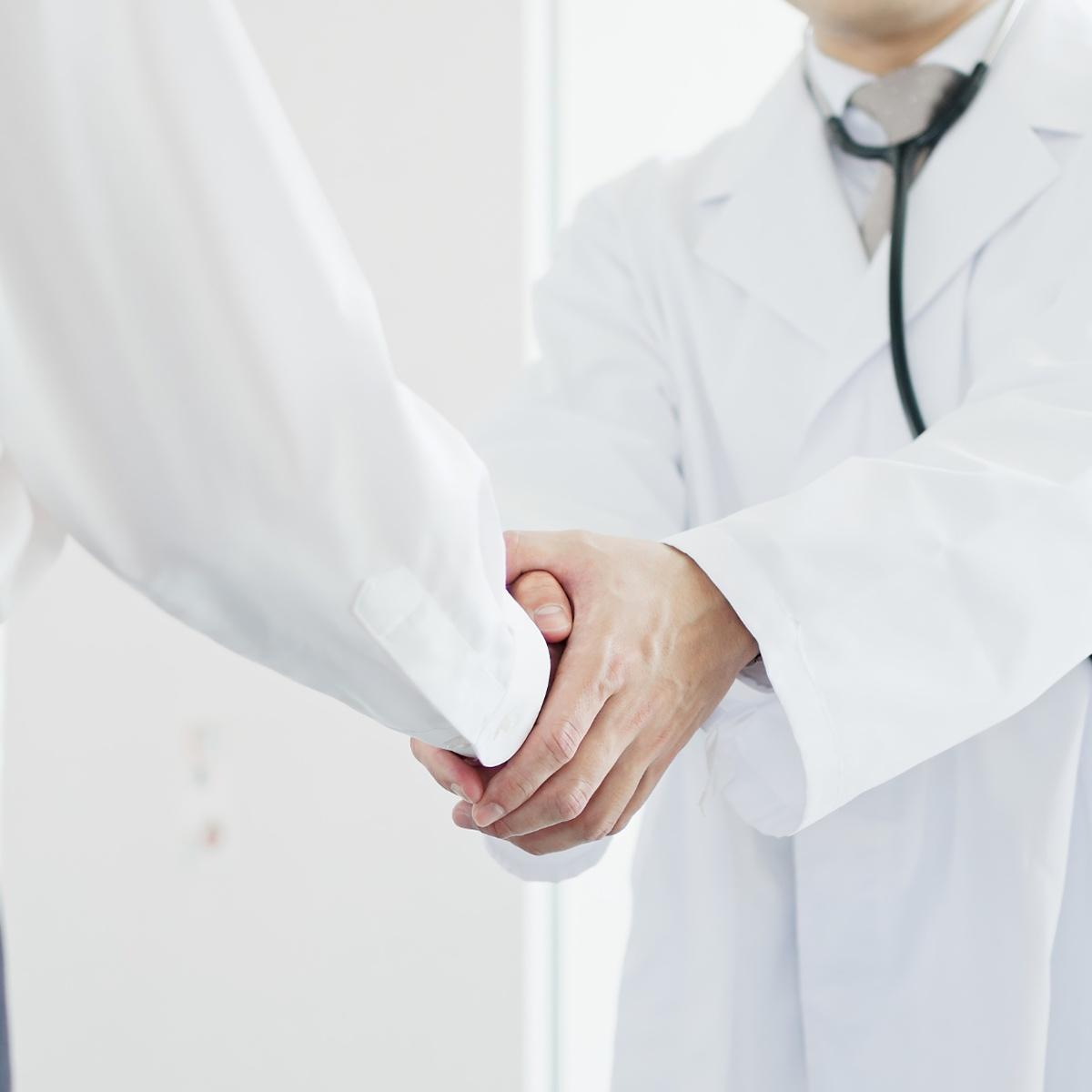 person in white coat and stethoscope shaking hand of person with white sleeve