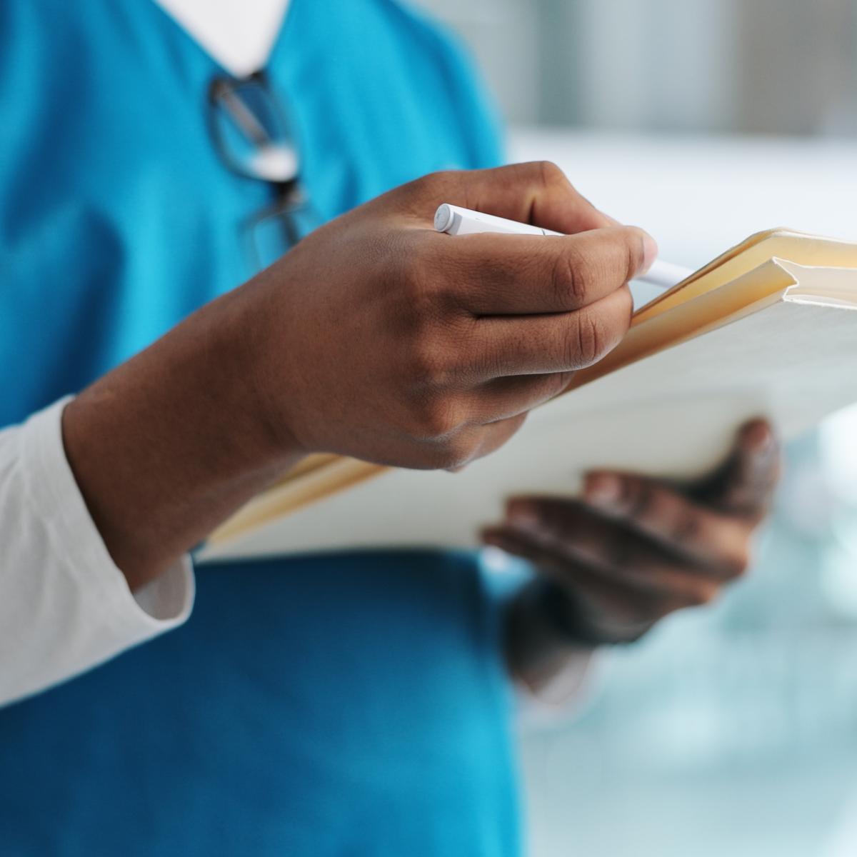 Close-up of a healthcare professional’s hand, writing in a notebook.